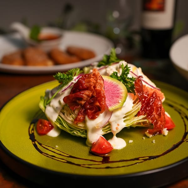 Wedge salad with bacon, tomatoes, radish, and creamy dressing on a green plate at Il Forno a Legna.