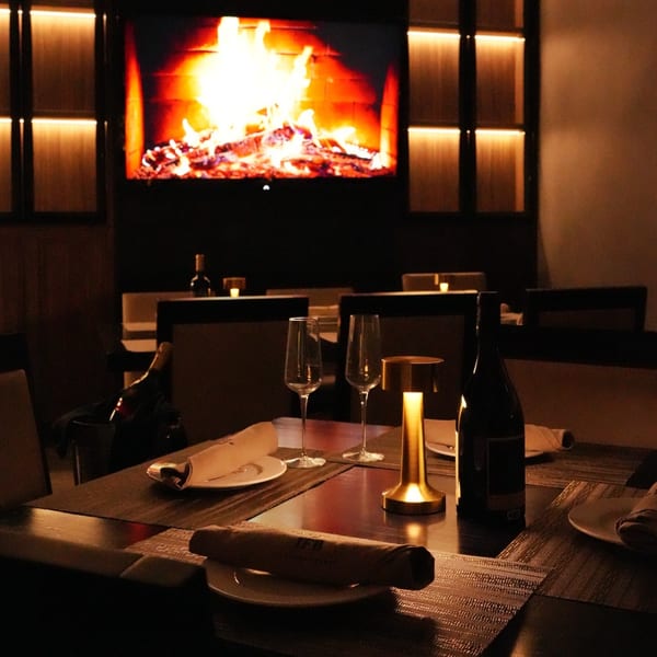 A dark, intimate dining room at Il Forno a Legna with a table set for two and a large fireplace.