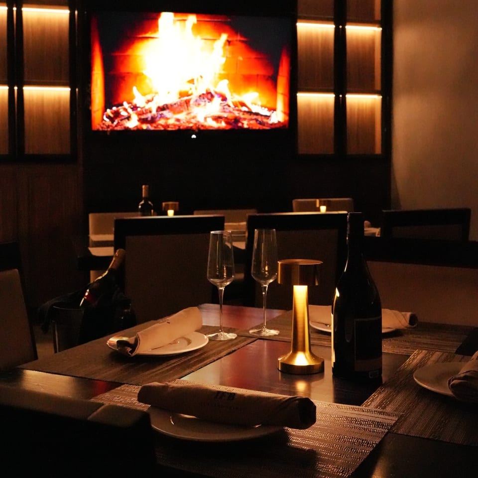 A dark, intimate dining room at Il Forno a Legna with a table set for two and a large fireplace.