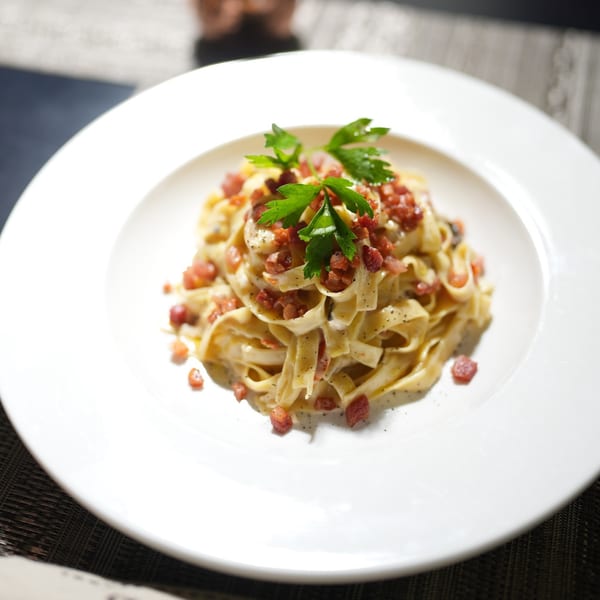Creamy fettuccine pasta with crispy bacon bits and fresh parsley on a white plate.
