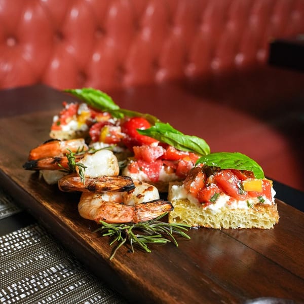 Grilled shrimp and tomato bruschetta with basil and rosemary on a wooden board.