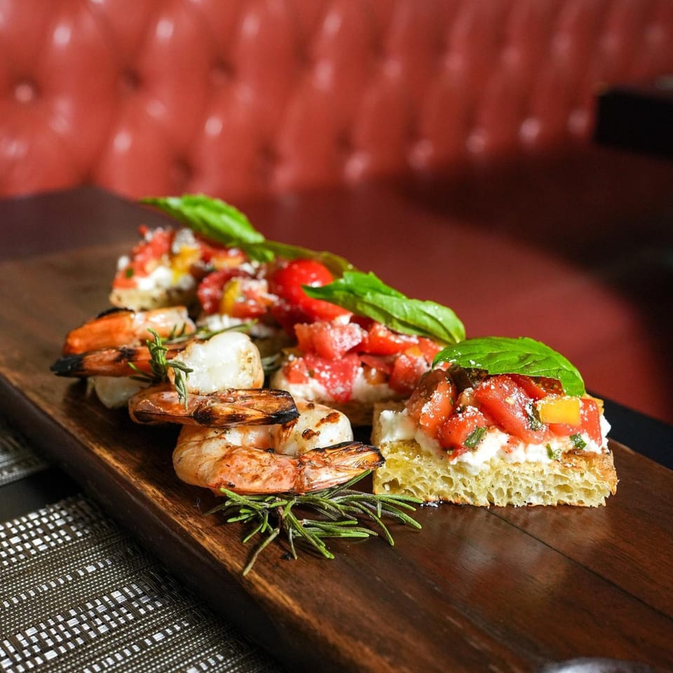 Grilled shrimp and tomato bruschetta with basil and rosemary on a wooden board.