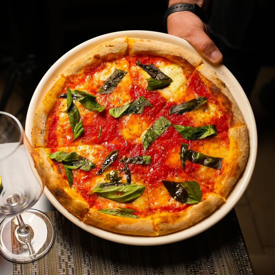 Margherita pizza with tomato sauce, melted cheese, and fresh basil served on a white plate at a restaurant table.