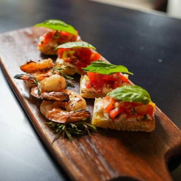 Grilled shrimp and bruschetta with tomatoes, cheese, and basil on a wooden board.