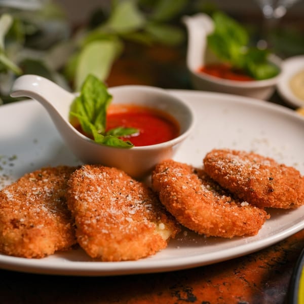 Four crispy, breaded mozzarella sticks with parmesan, served with a side of marinara sauce and basil.